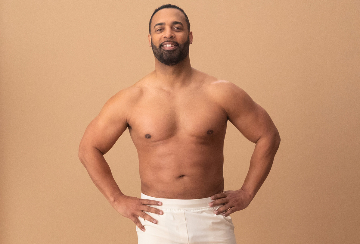 Man smiling confidently, standing with hands on hips against a tan background.