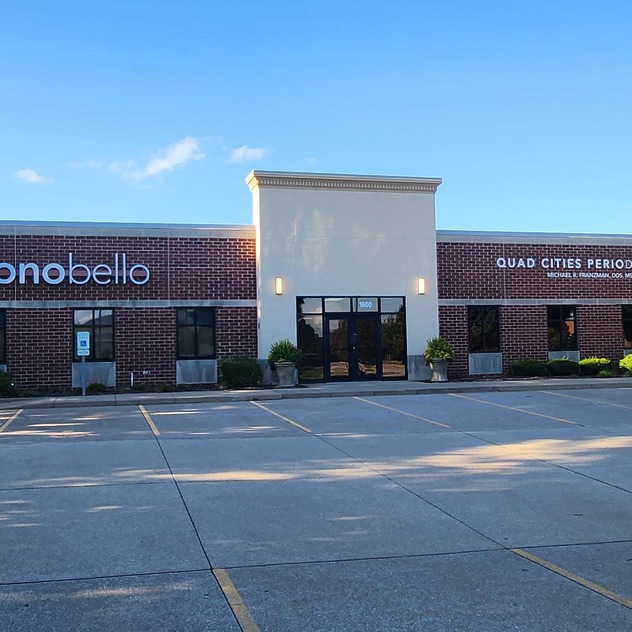 Exterior view of a brick building with Sono Bello and Quad Cities Periodontics signage on a sunny day.