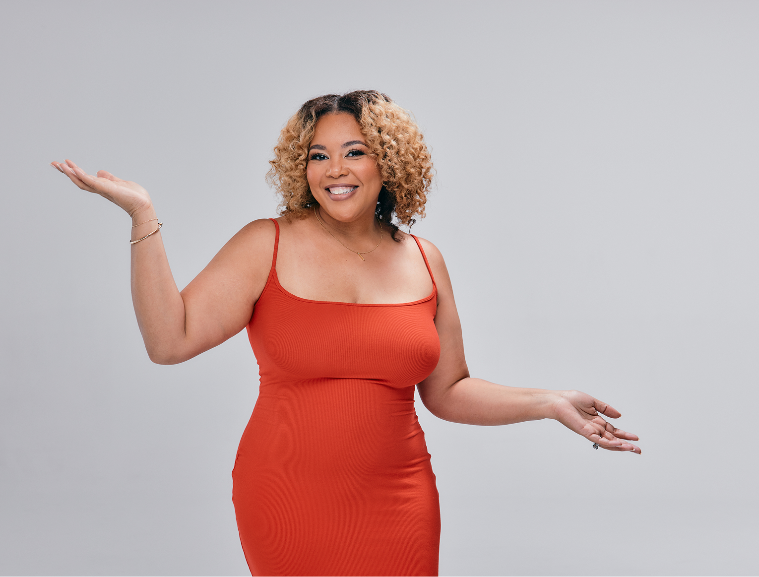 Person in a red dress smiling with arms outstretched against a plain background.