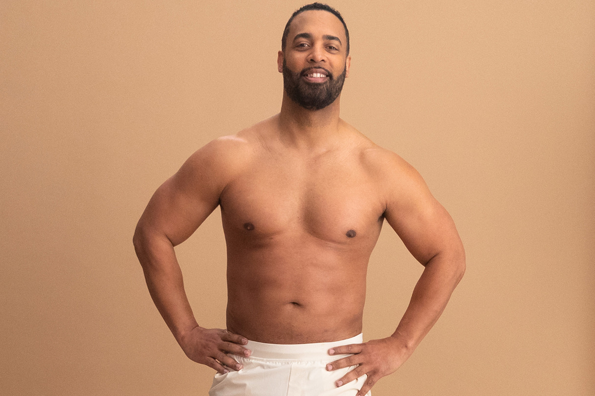 Man posing confidently against a neutral background, wearing light-colored pants.