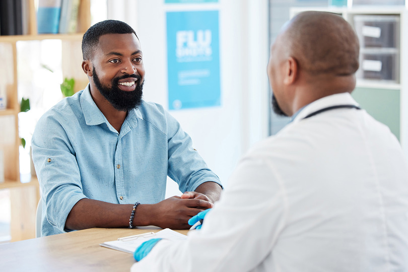 Man smiling while talking to a doctor in an office setting, with a flu awareness poster visible in the background.