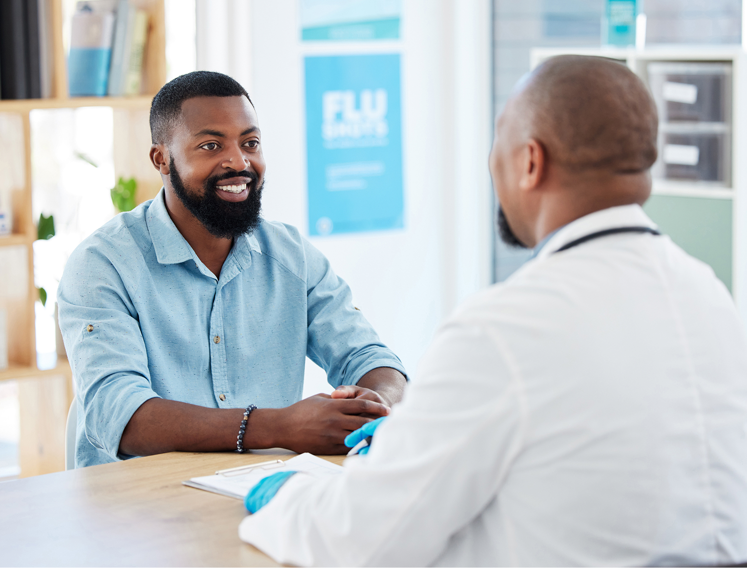 Man smiling while talking to a doctor in an office setting, with a flu awareness poster visible in the background.