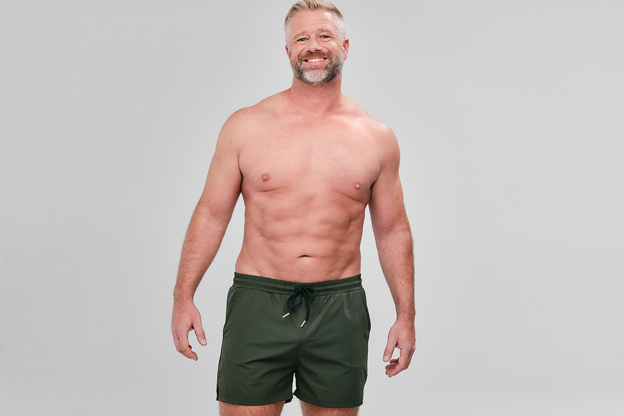 Man with a smile wearing green shorts against a plain background.