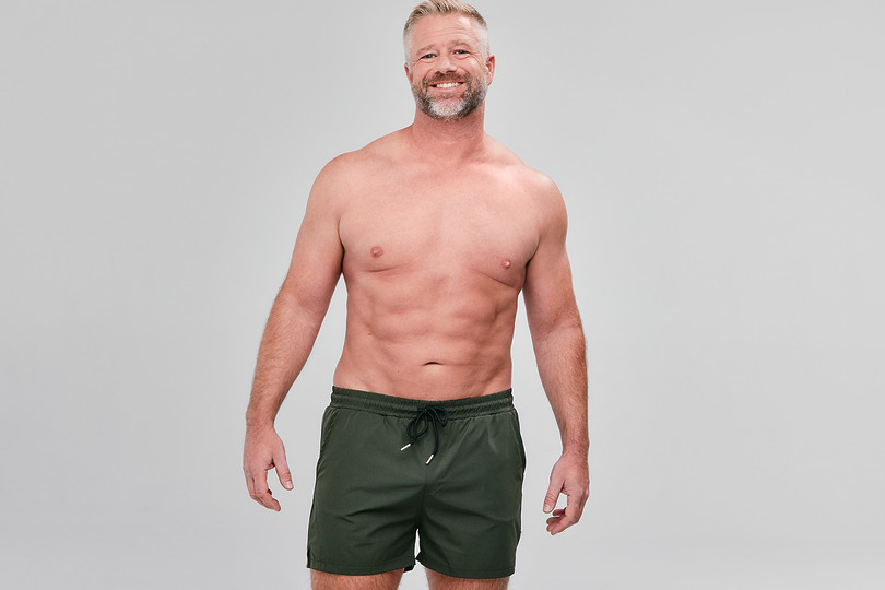 Man with a smile wearing green shorts against a plain background.