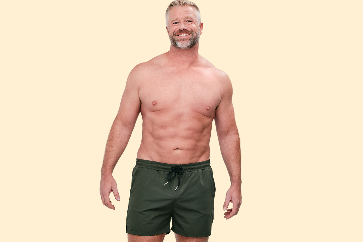 Man in black shorts smiling against a beige background