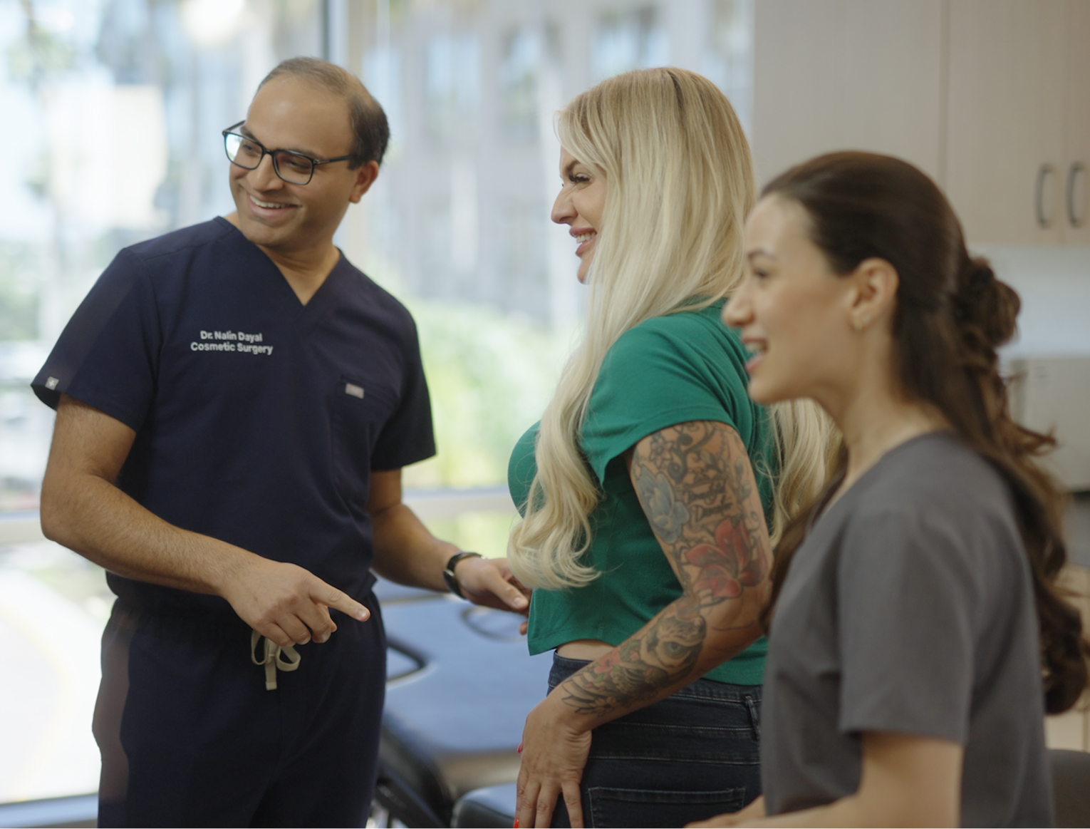 Group of three people smiling and talking in a bright office setting, one wearing medical scrubs.