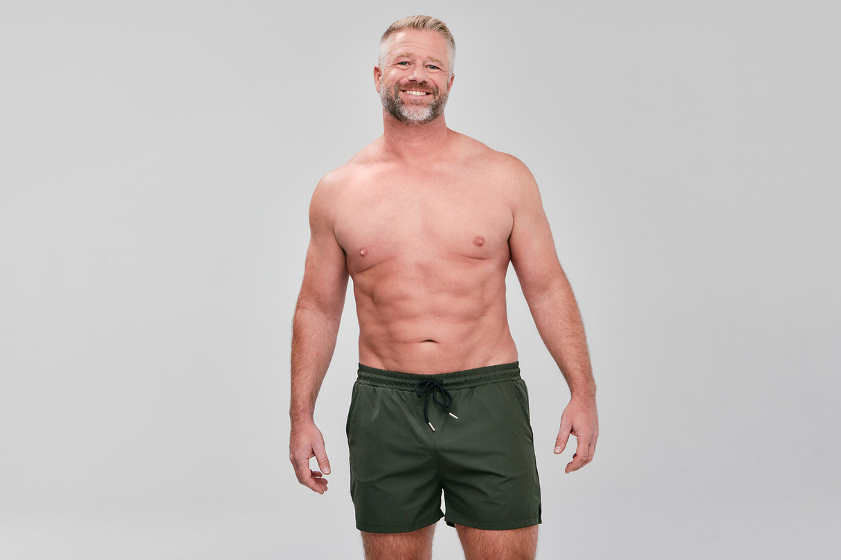 Man with a beard smiling, wearing green shorts against a plain gray background.