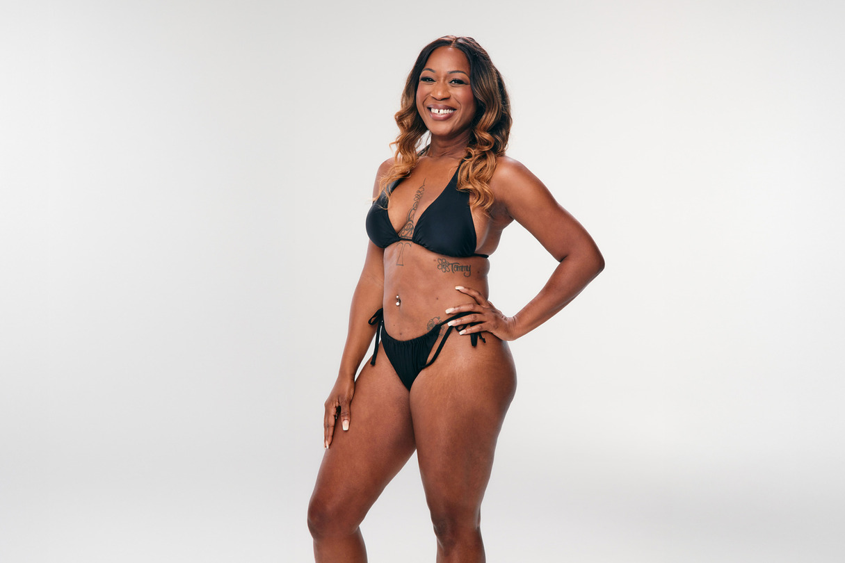 Smiling person in a black bikini standing in front of a plain white background.
