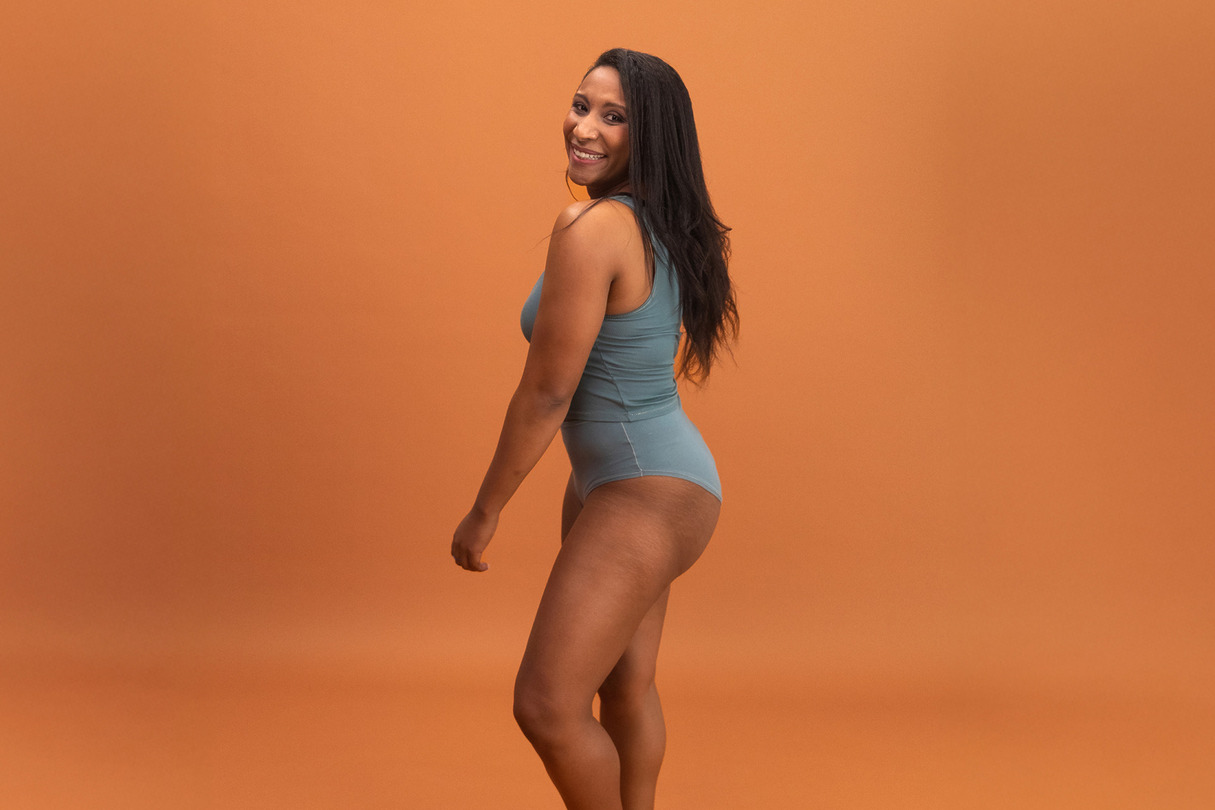 Person posing confidently in teal athletic wear on a warm orange background.