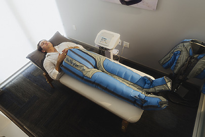 Person lying on a treatment table wearing blue compression therapy pants in a wellness clinic.