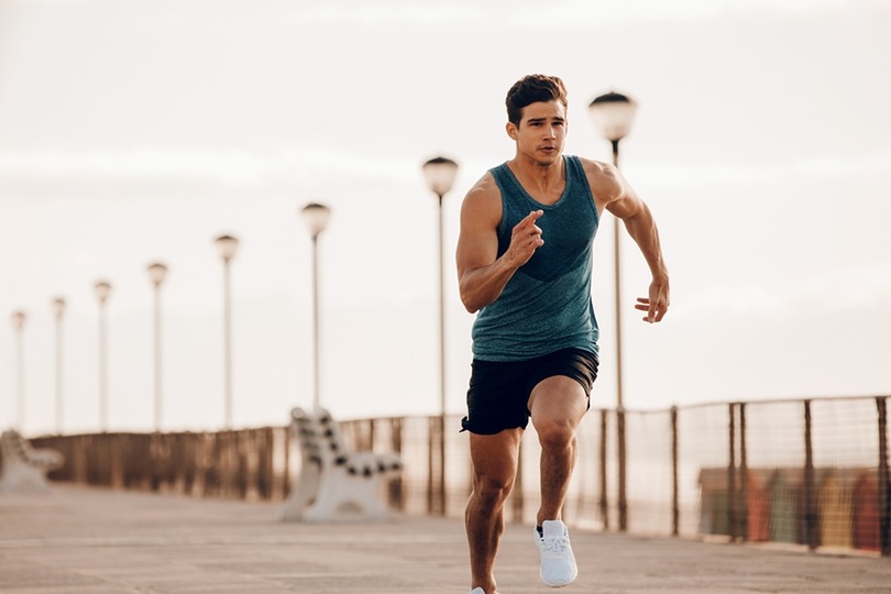 Man in athletic wear running on a boardwalk lined with street lamps and empty benches, early morning exercise routine.