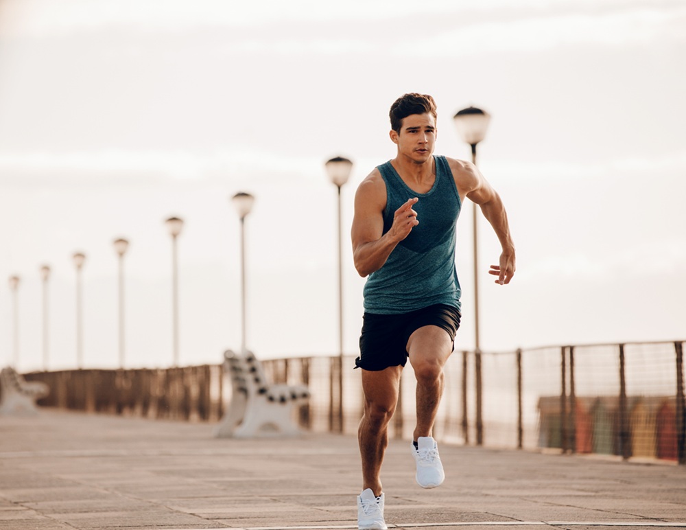 Man in athletic wear running on a boardwalk lined with street lamps and empty benches, early morning exercise routine.