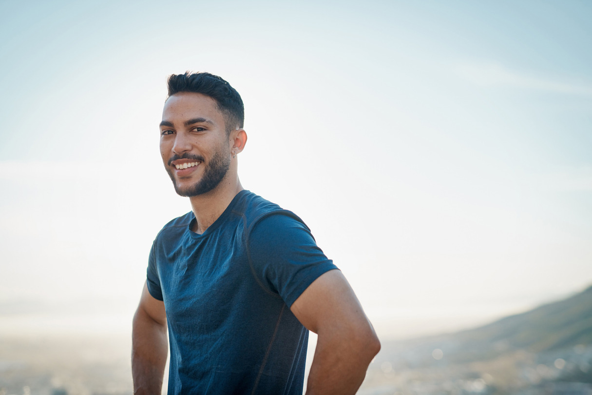 Man smiling outdoors with a blue sky background.