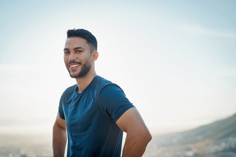 Man smiling outdoors with a blue sky background.