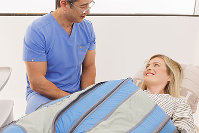 Person in medical scrubs assisting a patient using a leg compression therapy device in a clinic setting.