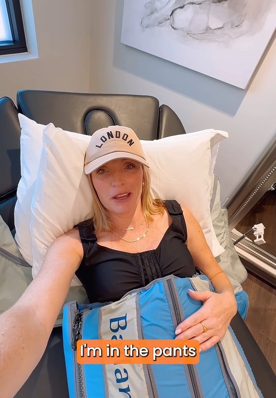 Person relaxing in a recliner, wearing a cap and using a compression therapy device.