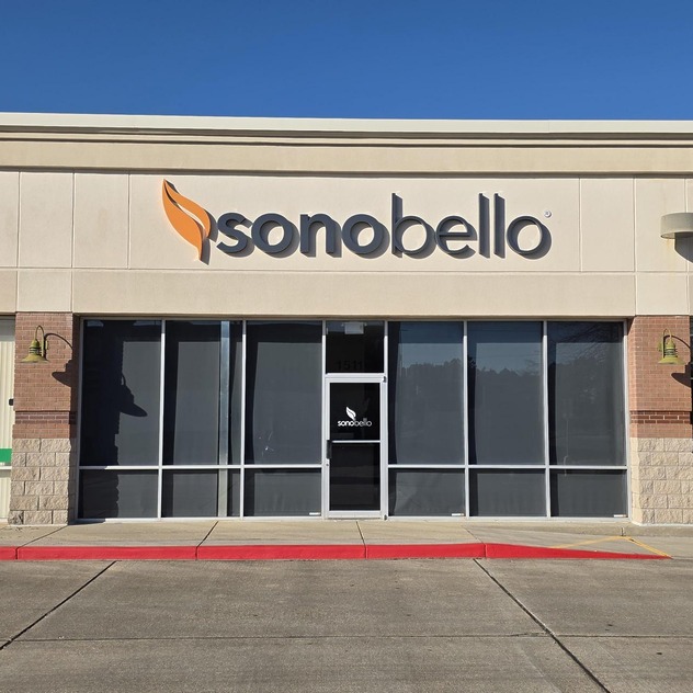 Front view of Sono Bello clinic with large logo on a sunny day in a shopping center.