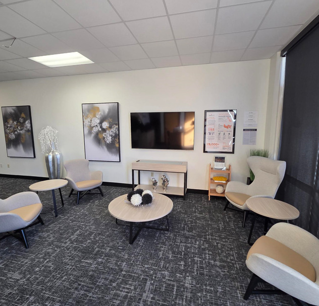 Modern office waiting area with minimalist decor, featuring comfortable chairs, tables, and wall art.