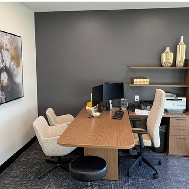 modern office with a wooden desk, chairs, dual monitors, abstract wall art, shelves, and decorative vases