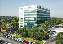 Aerial view of a modern Sono Bello office building surrounded by parked cars and green trees on a sunny day.
