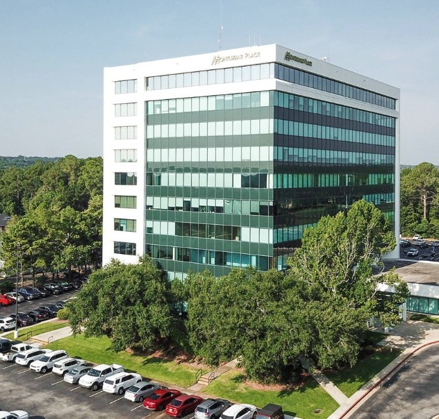 Aerial view of a modern Sono Bello office building surrounded by parked cars and green trees on a sunny day.