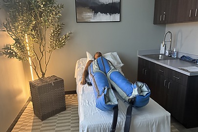 Person lying on a treatment bed with compression therapy sleeves in a calm room with a plant and wall art.