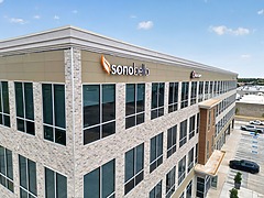 Exterior view of a modern office building with large windows and the Sono Bello logo on the facade.