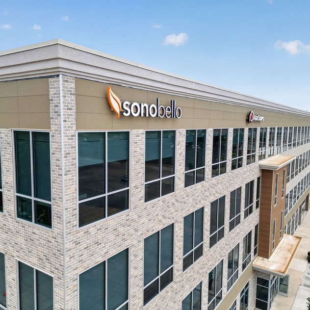 Exterior view of a modern office building with large windows and the Sono Bello logo on the facade.