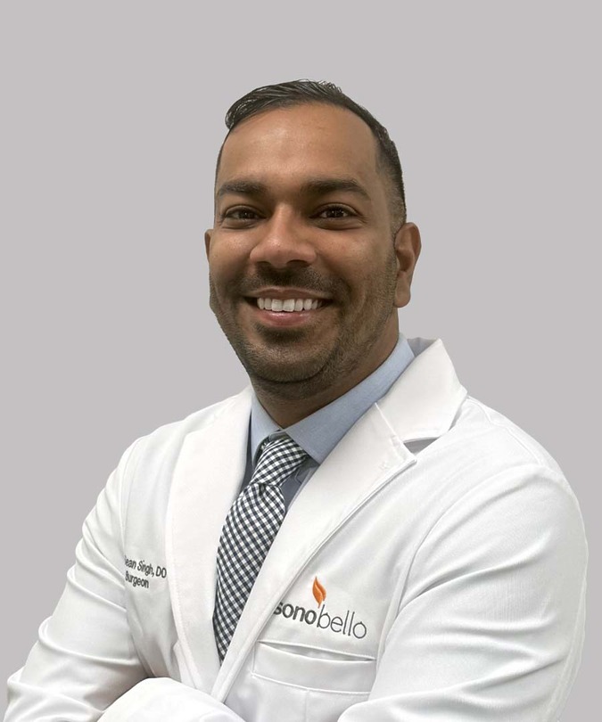 Smiling doctor in a white coat with folded arms against a plain background.