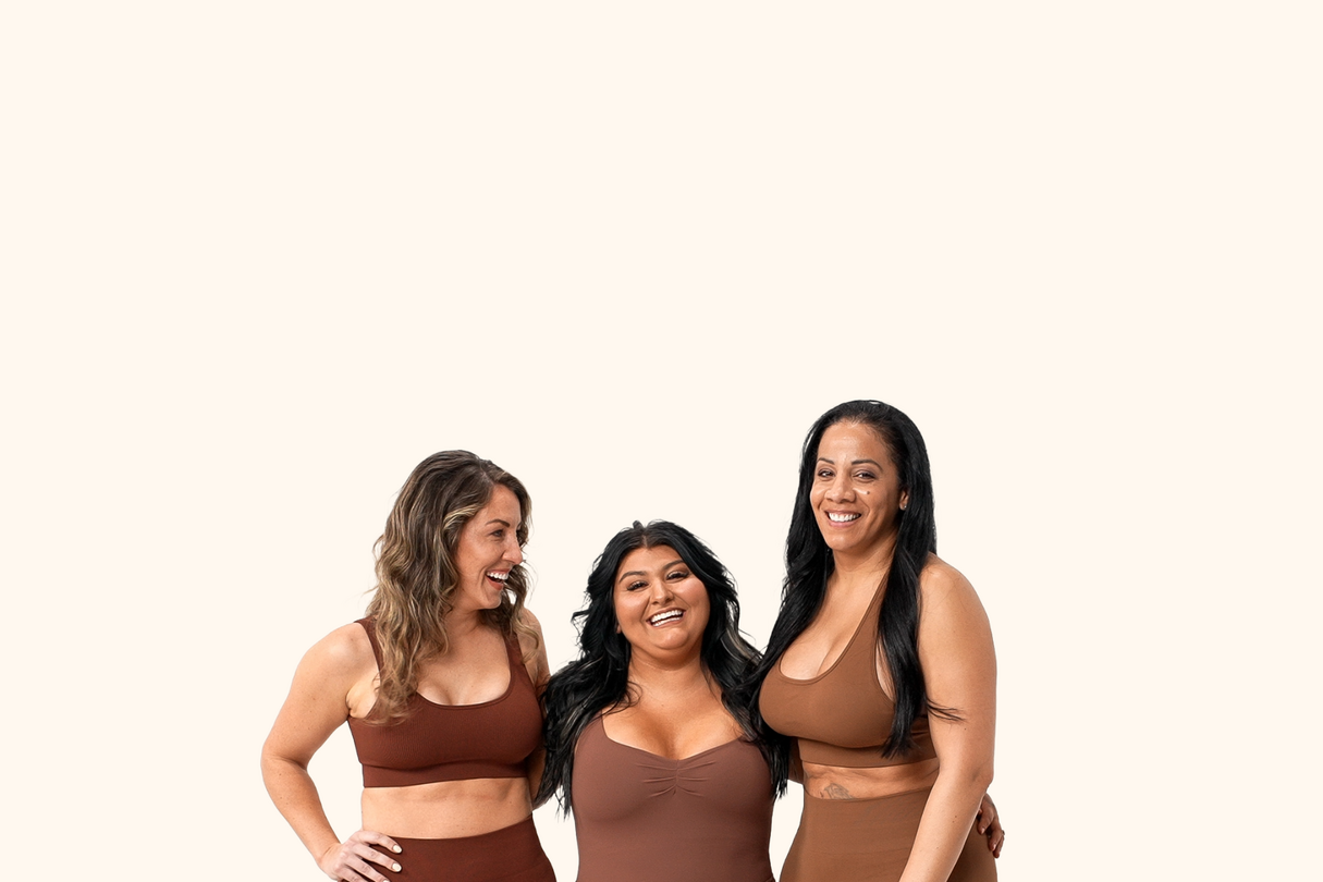 Three women smiling and standing together, wearing activewear in shades of brown against a light background.