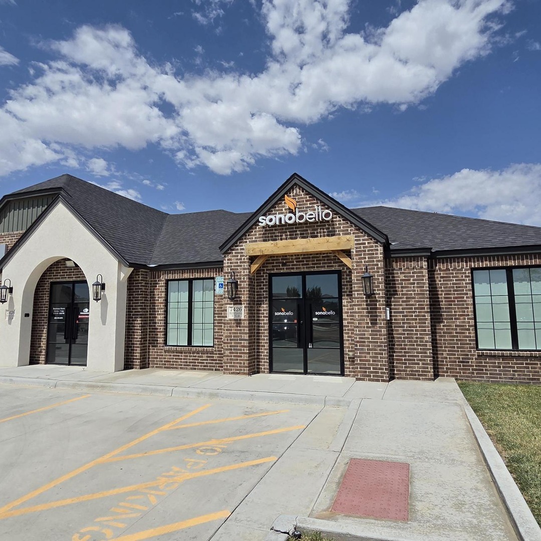 Exterior of a brick building with large windows, a distinctive entrance, and a clear sky above.