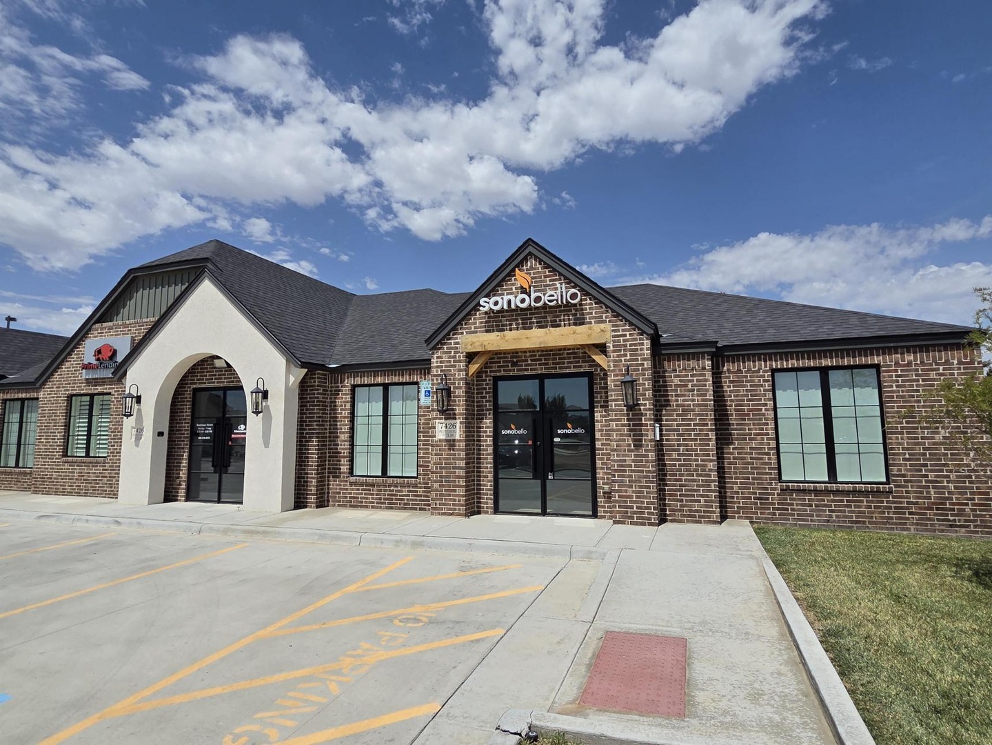 Exterior of a brick building with large windows, a distinctive entrance, and a clear sky above.